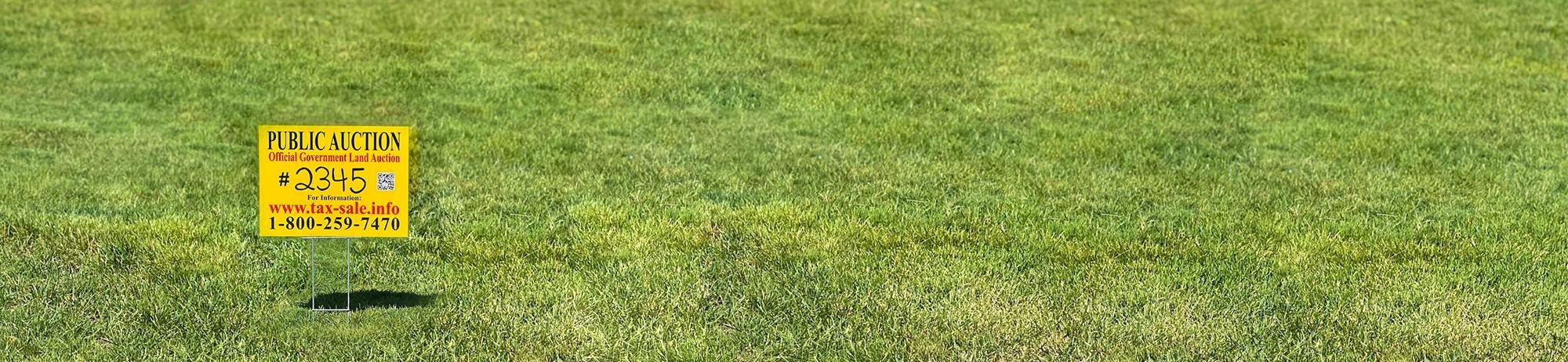 A yellow auction sign on a lawn.